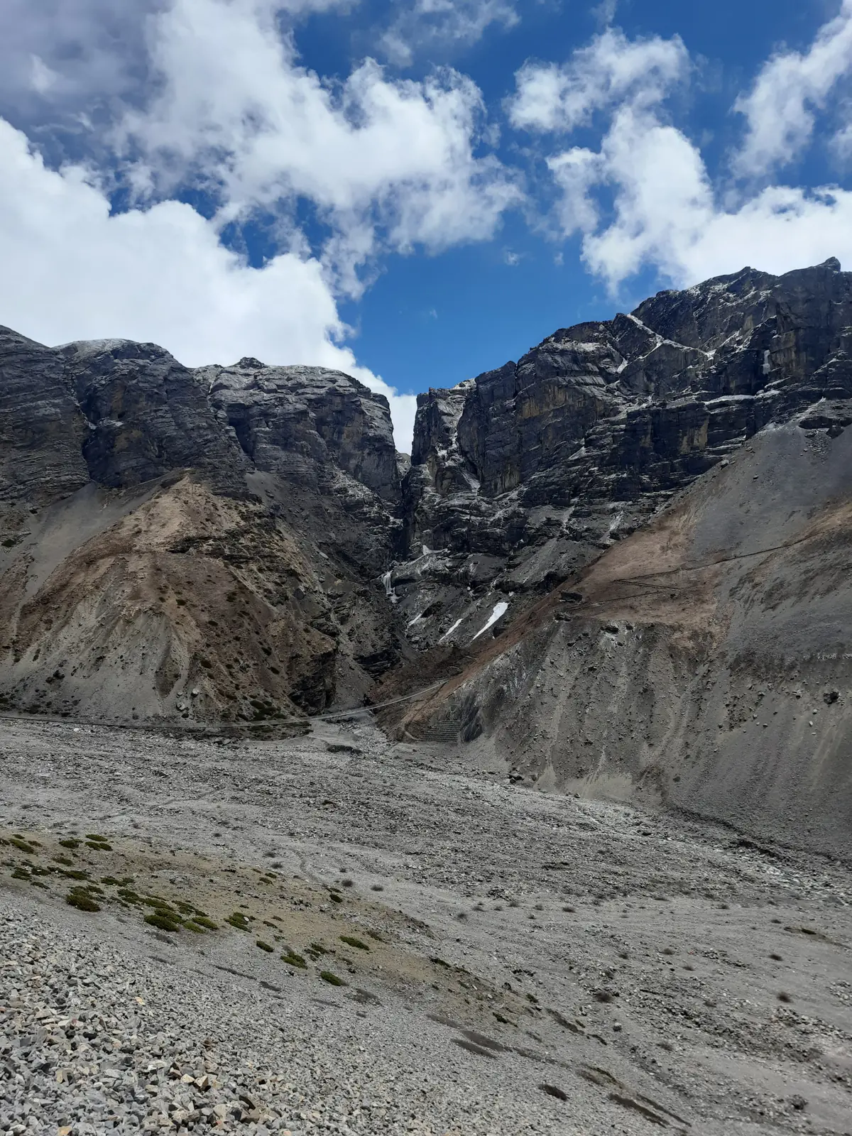 Eroded canyon walls above a wide gravel bed with a waterfall in the cleft