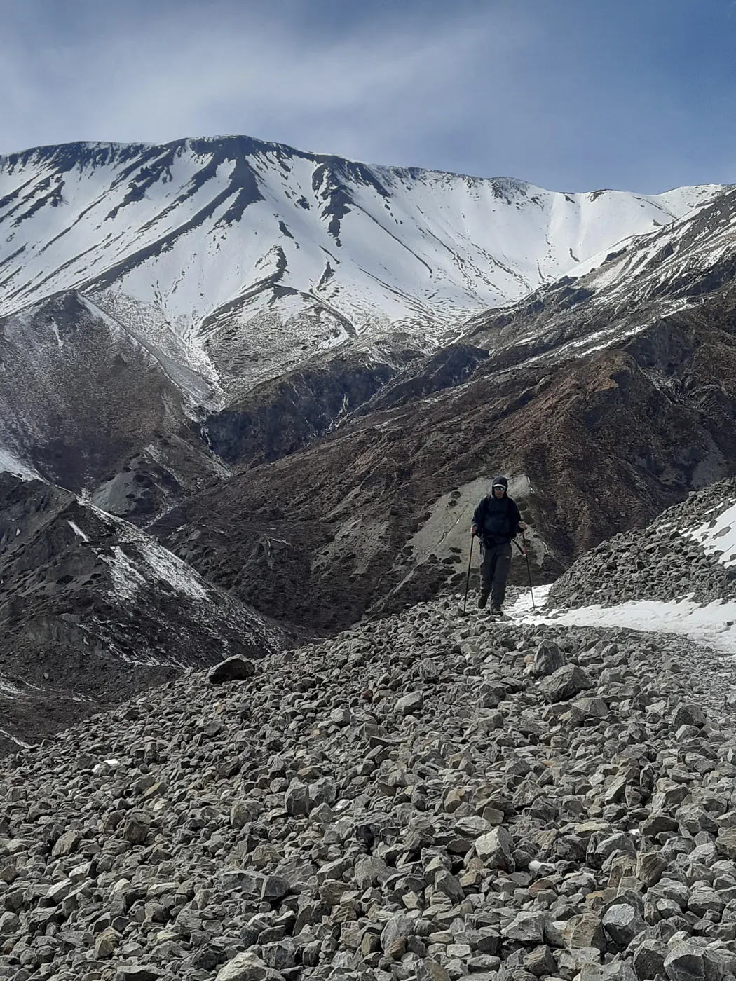 Trekker descending a boulder field below a snow-covered ridge