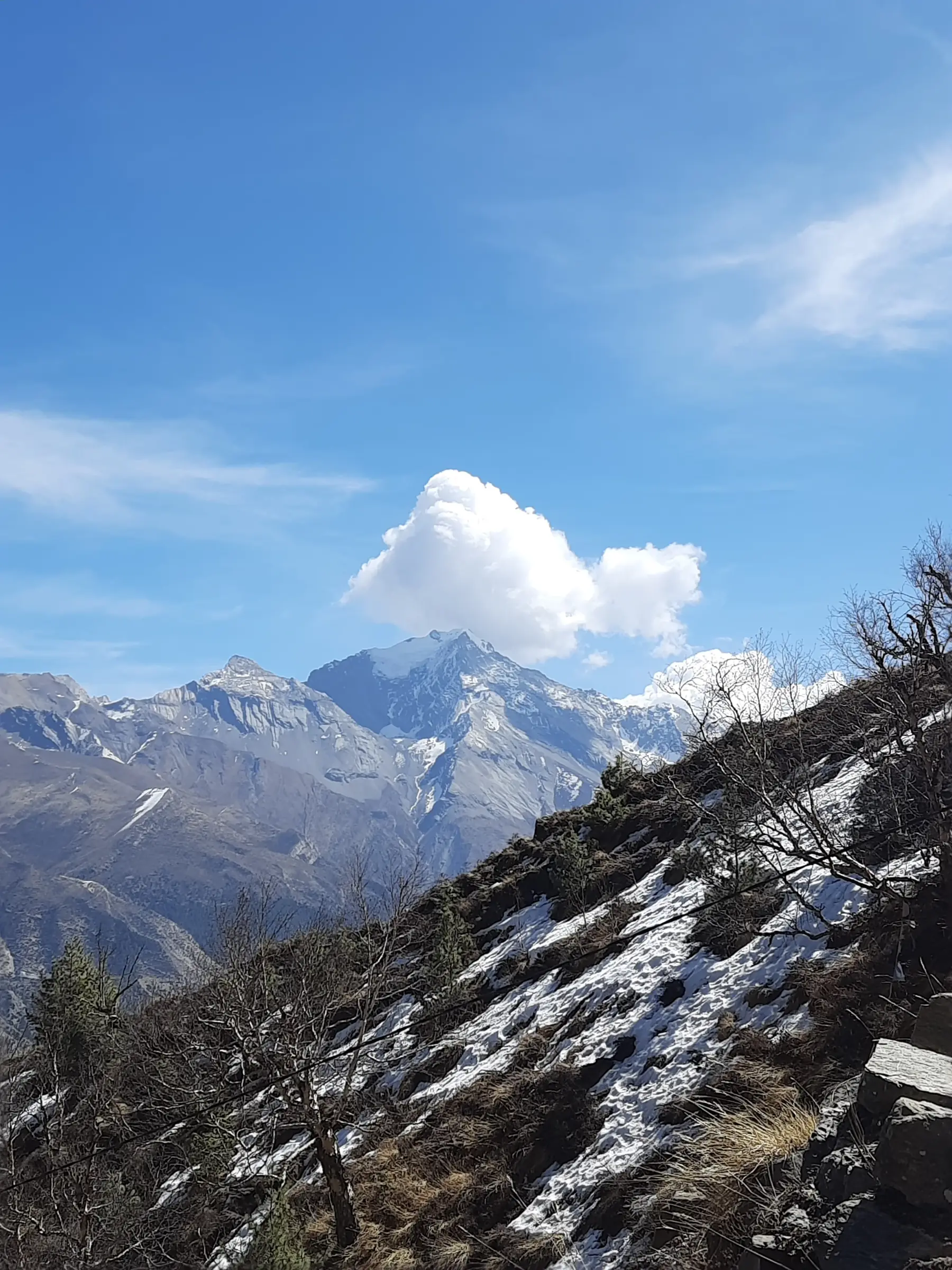 A high ridge trail under a clear blue sky with snow peaks beyond